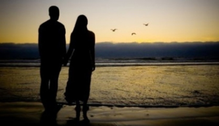 Zamilovaný pár stojící na pláži a sledující západ slunce