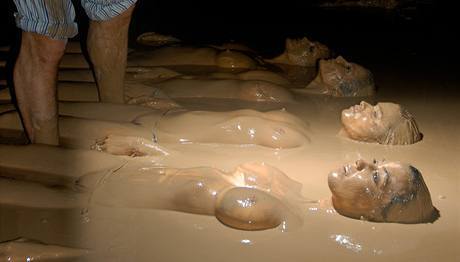 Muž fotí nahé ženy ležící v bahně